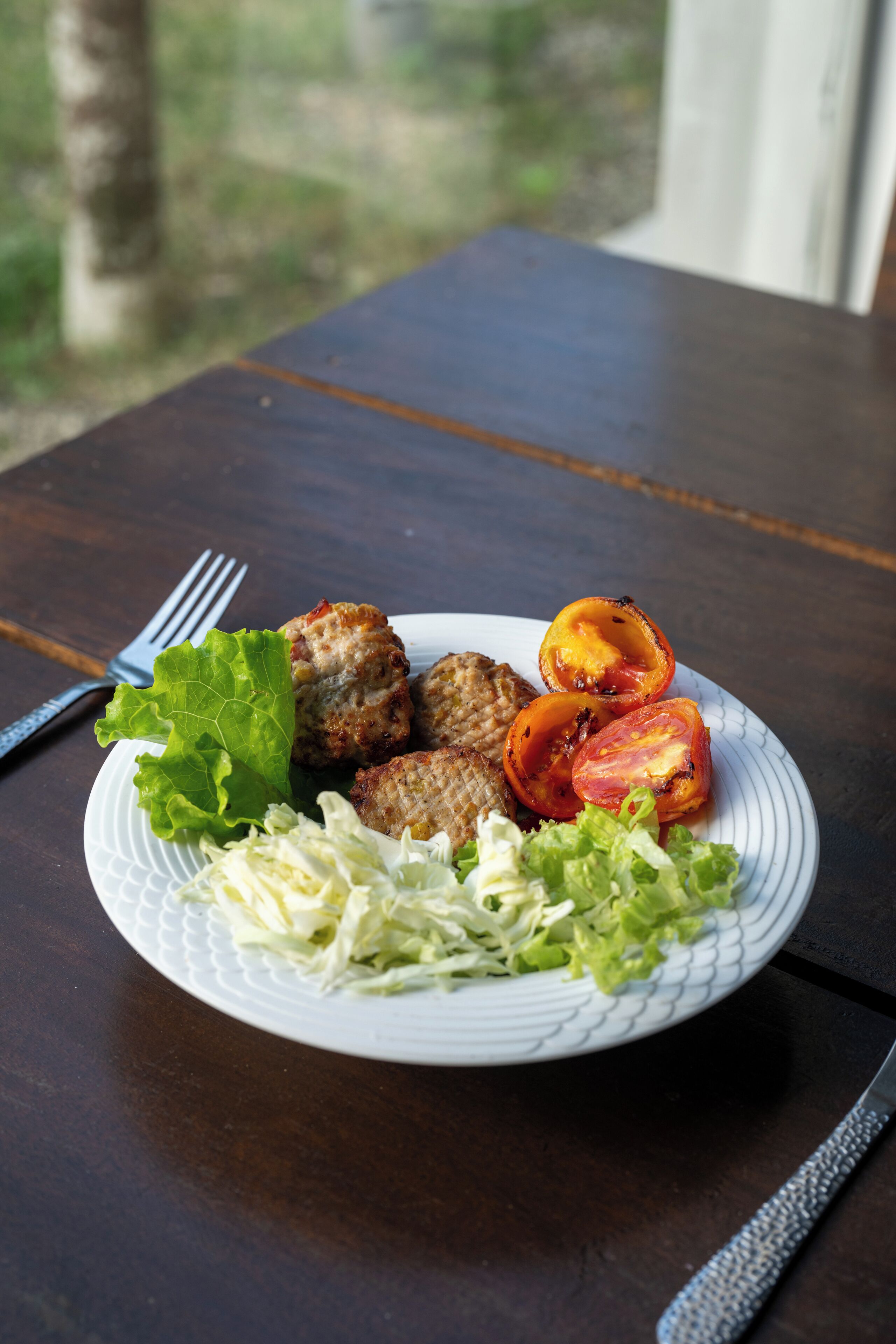 A plate of food with meatballs, tomatoes, and lettuce on a table.