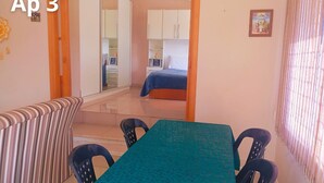 A room with a dining table, chairs, a striped sofa, a bed, and a wardrobe.