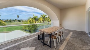 Un balcon avec une table et des chaises, donnant sur un terrain de golf bordé de palmiers.