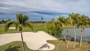 Un parcours de golf avec des bunkers de sable, des palmiers et un plan d’eau.