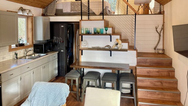 Cocina compacta con comedor, escalera de madera y pequeño rincón de estar.