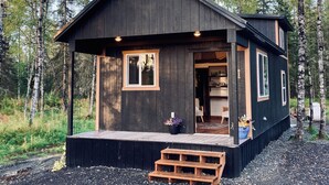 Una cabaña con porche, terraza de madera y un pequeño espacio exterior con mobiliario.