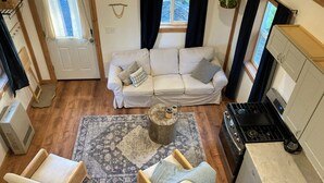Un salón acogedor con un sofá, dos sillones, una mesita de centro y una alfombra.  Incluye una zona de cocina con estufa y armarios.