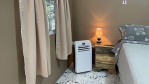 A bedroom with a bed, a bedside table with a lamp, a heater, and a window with curtains. - Modern 1-bedroom apartment with AC, WiFi and Kitchen in beautiful Negril . (Negril)