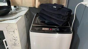 A white washing machine with a digital display, a black pan on a white countertop, and a beige curtain in the background. - Modern 1-bedroom apartment with AC, WiFi and Kitchen in beautiful Negril . (Negril)