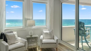 A room with two armchairs, a lamp, and a view of the ocean through large windows.