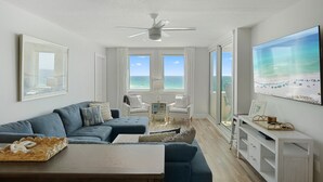 A modern living room with a large window, a ceiling fan, and a view of the ocean.