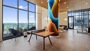 A modern interior with large windows, a central column with a colorful design, and a minimalist furniture arrangement. - Luxury Rainey St Condo with rooftop pool, Lakeview & Gym (Austin)