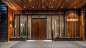 A modern hotel entrance with a wooden facade, glass doors, and a neon sign. - Luxury Rainey St Condo with rooftop pool, Lakeview & Gym (Austin)