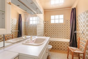 Ein Badezimmer mit Waschbecken, Toilette und Badewanne, Wänden mit Muster und einem Fenster.