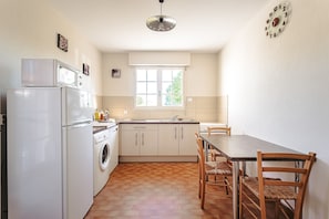A kitchen with a refrigerator, washing machine, wooden dining table, and chairs.