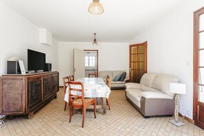 Ein Wohnzimmer mit Esstisch, Stühlen, einer Couch, einem Fernseher und einem Schrank.