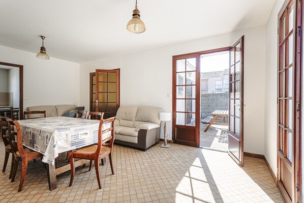 Une pièce comprenant une table à manger, des chaises, un canapé, une lampe et une porte-fenêtre coulissante donnant sur un espace extérieur.