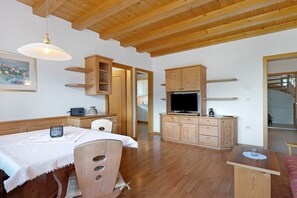 A spacious room with a wooden ceiling, a dining table with chairs, a television, and wooden cabinets. - Apartment 'Hofanger Meran' with Mountain View, Balcony and Wi-Fi (Algund)
