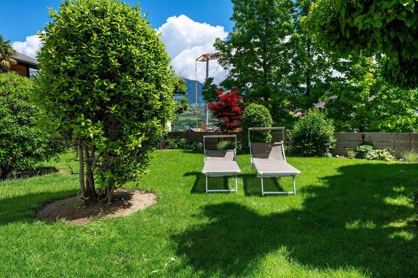 A grassy outdoor area with two lounge chairs and a tree.