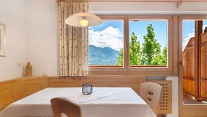 A wooden dining table with a white tablecloth, a candle, and a view of mountains through large windows. - Apartment 'Hofanger Tirol' with Mountain View, Balcony and Wi-Fi (Algund)