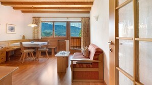 A cozy room with wooden furniture, a dining table, a sofa, and large windows offering a mountain view. - Apartment 'Hofanger Tirol' with Mountain View, Balcony and Wi-Fi (Algund)