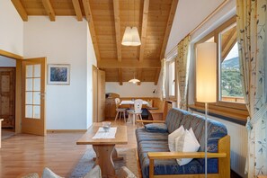 Un intérieur chaleureux avec un plafond en bois, un canapé, une table à manger et une vue sur l’extérieur.
