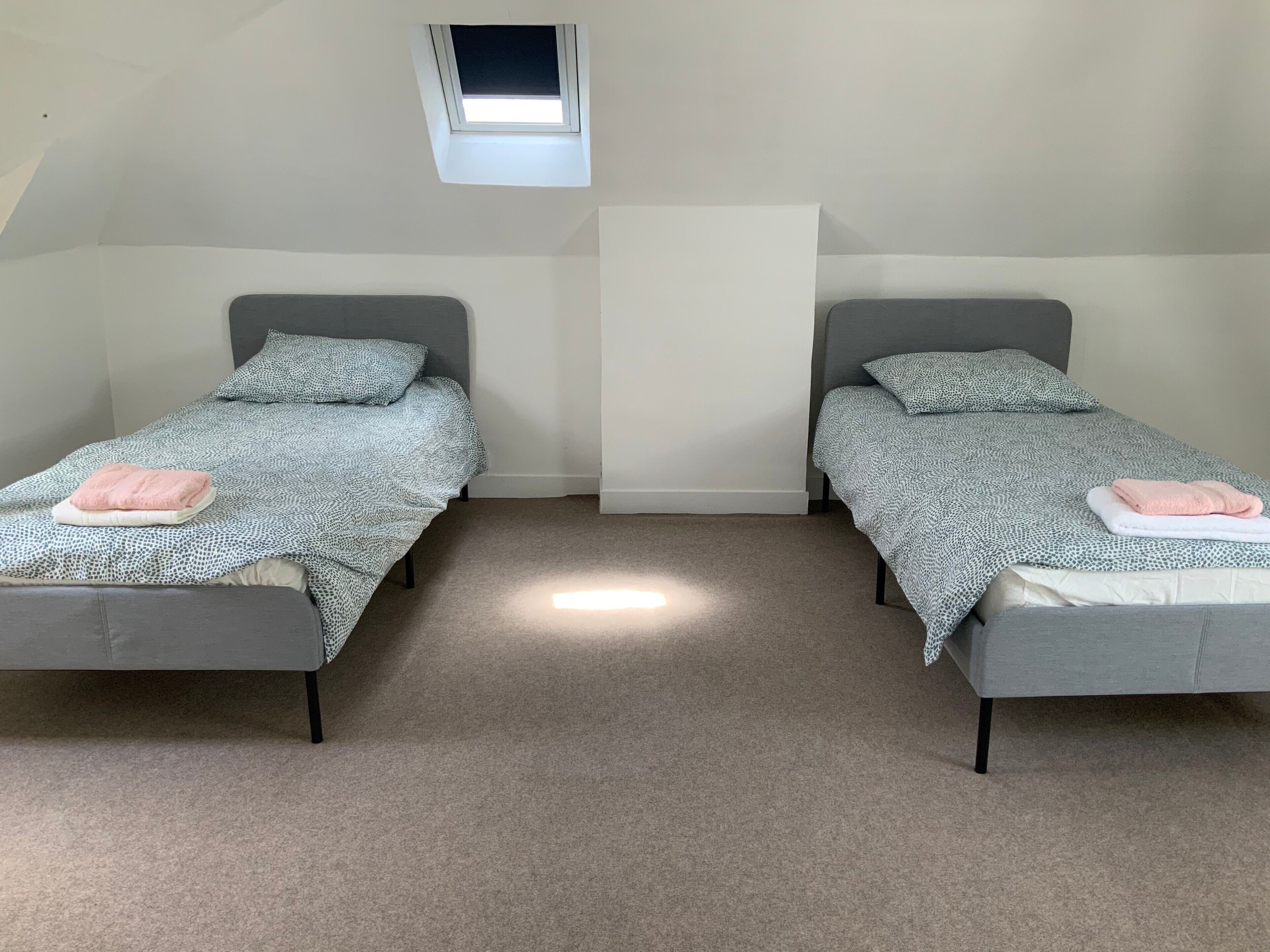 Una habitación con dos camas individuales, una ventana pequeña y piso alfombrado.