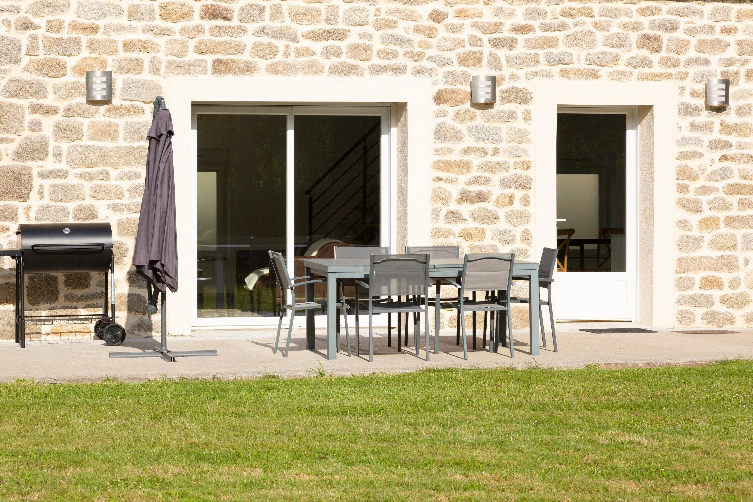 A stone building with a patio area featuring a grill, outdoor seating, and a staircase leading to an upper level.