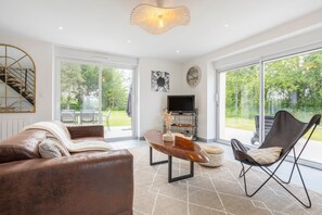 A spacious living room with a leather sofa, a wooden coffee table, a black chair, and a TV.