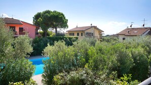 A residential area with a swimming pool surrounded by dense greenery, houses with red and yellow exteriors, and a large tree in the center.