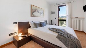 A bedroom with a bed, bedside table, wall art, and a view through a window.