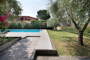 Une piscine dotée d’une plage en pierre, entourée d’un jardin bien entretenu avec différentes espèces de plantes et une haie.
