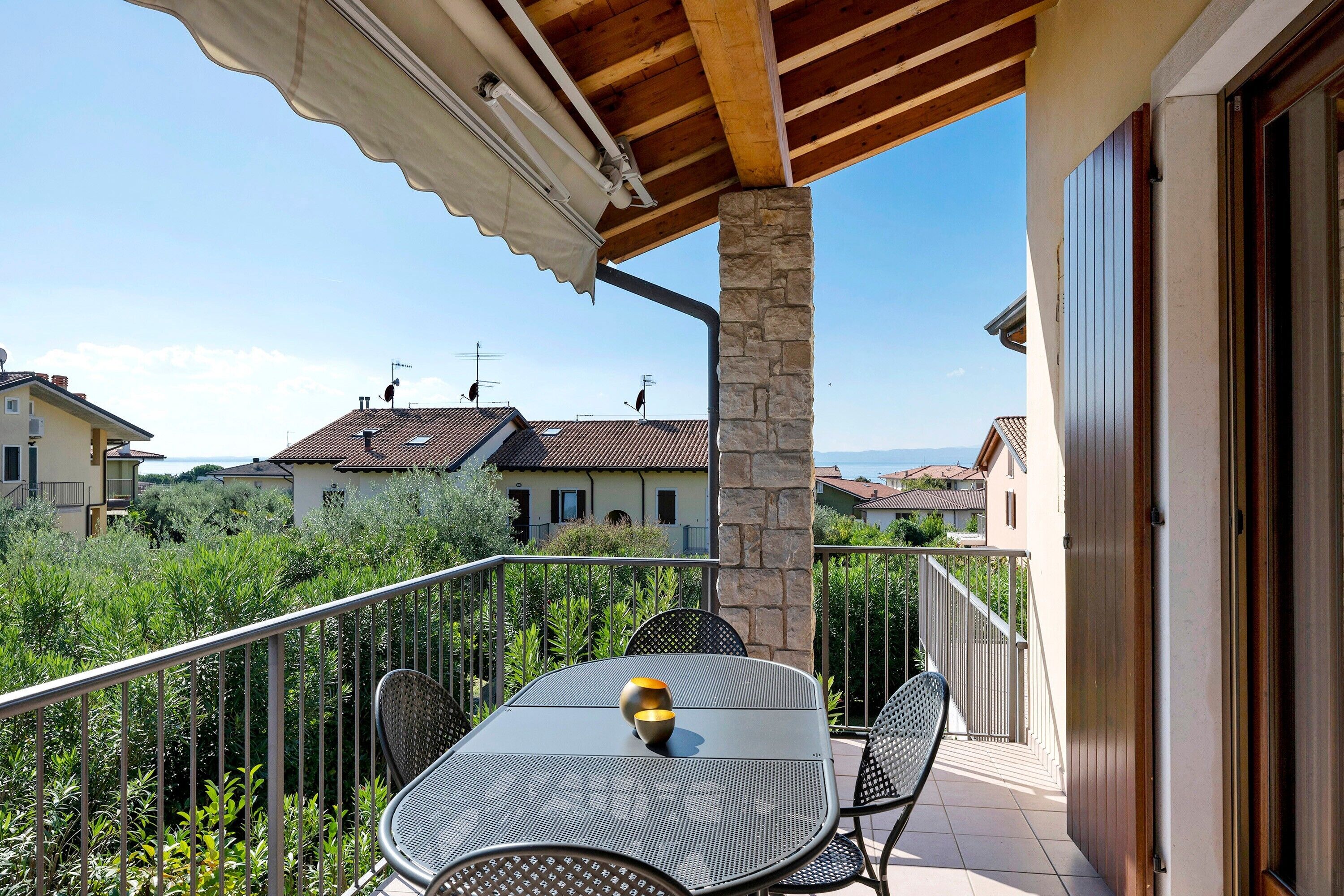 A balcony with a table and chairs, a stone pillar, and a view of houses in the background.