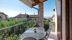 A balcony with a table and chairs, a stone pillar, and a view of houses in the background.