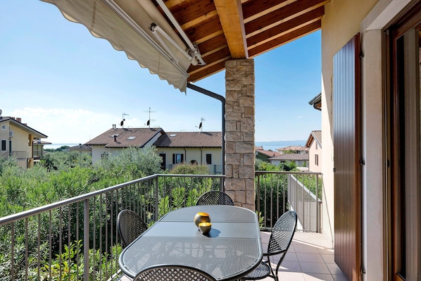 Un balcon avec une table et des chaises, un pilier en pierre et une vue sur des maisons en arrière-plan.