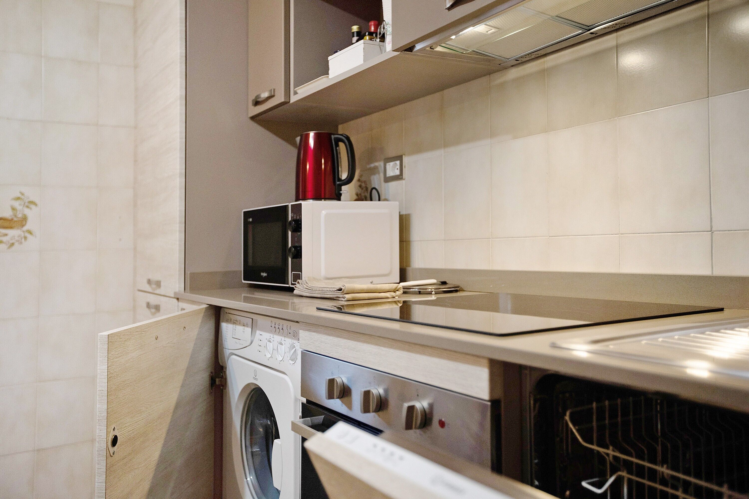 A compact kitchen with a microwave, a red coffee pot, and a washing machine.