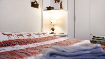 Ein Schlafzimmer mit einem Bett, einer Nachttischlampe, einem an der Wand befestigten Regal mit Dekorationen und einem Kleiderschrank.