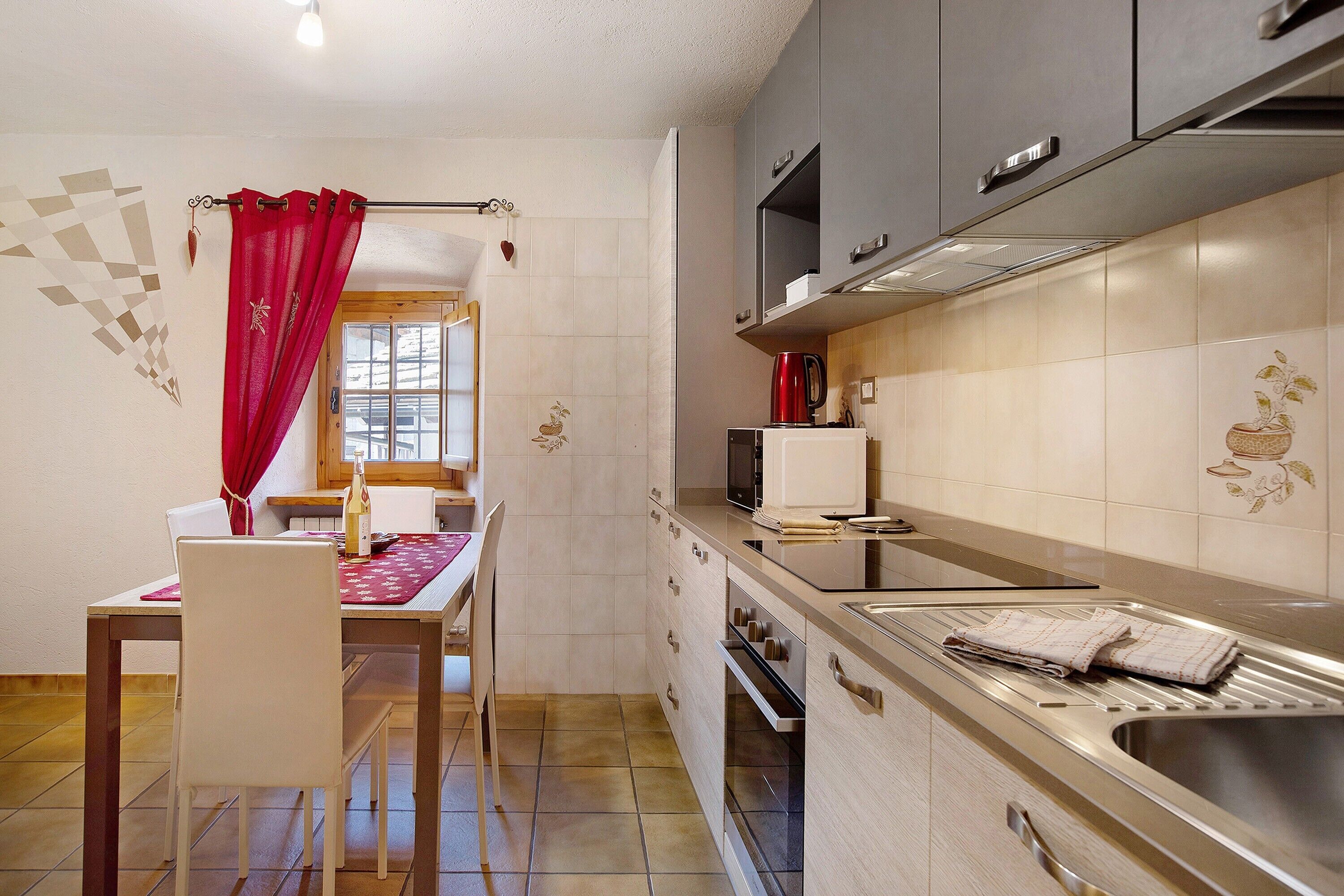 A compact kitchen with a dining area, a red curtain, and a tiled backsplash.