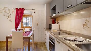 A compact kitchen with a dining area, a red curtain, and a tiled backsplash.