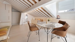 Quarto de loft moderno com teto inclinado, mesa de jantar redonda com cadeiras e uma janela ampla.