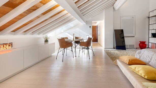 Quarto moderno no estilo loft com teto inclinado, área de jantar com mesa e cadeiras, e uma janela grande.
