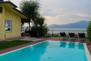 Piscina con vistas a montañas, un edificio amarillo y asientos al aire libre.