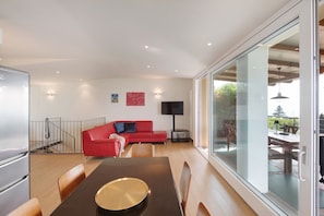 Un espacio habitable moderno con zona de comedor, sofá rojo, televisor de pantalla plana y un gran ventanal corredero que da a un área exterior.