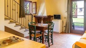 A dining area with a table, chairs, a fireplace, a television, and a staircase. - Apartment 'Cesare' with Shared Pool, Wi-Fi and Air Conditioning (Campiglia Marittima)