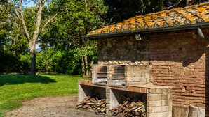 A rustic stone building with a tiled roof, a brick chimney, and a fire pit area with logs. - Apartment 'Cesare' with Shared Pool, Wi-Fi and Air Conditioning (Campiglia Marittima)
