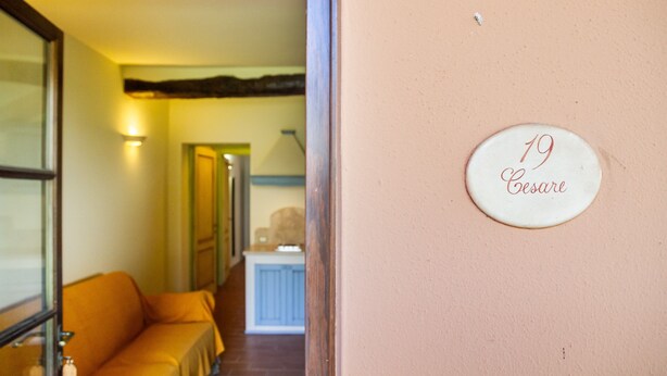 A hallway with a sofa, a door, and a wall with a number plaque. - Apartment 'Cesare' with Shared Pool, Wi-Fi and Air Conditioning (Campiglia Marittima)
