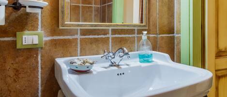 A bathroom with a white sink, a mirror, a towel, and a soap dispenser.