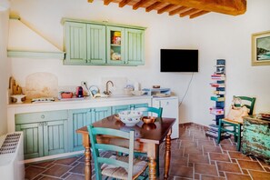 Cozinha com armários verdes, mesa de madeira e televisão fixada na parede.