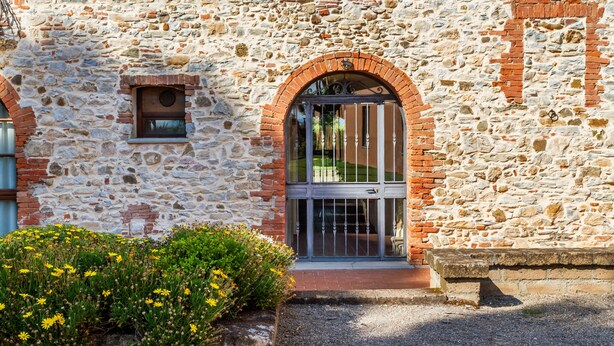 Un bâtiment en pierre avec un portail en métal, une petite fenêtre et un parterre de fleurs.