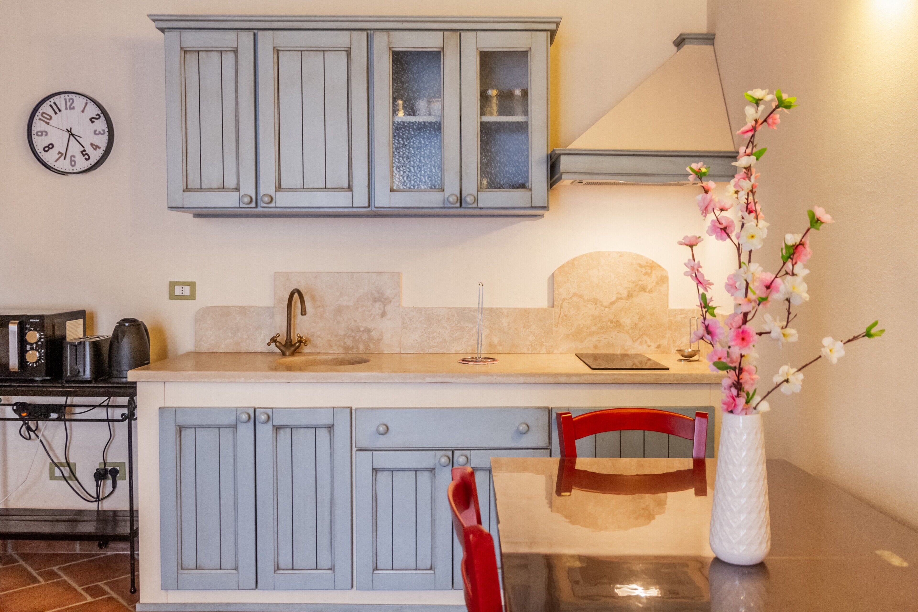 A kitchen with light blue cabinets, a sink, a clock, and a vase with flowers.