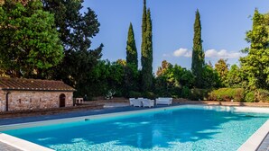 A clear swimming pool with white lounge chairs, surrounded by trees and a stone building.