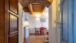 A hallway with a wooden door, a tiled floor, and a dining area with chairs and a table.