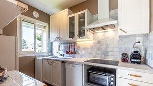 A compact kitchen with white cabinets, a dishwasher, a built-in oven, and a window providing natural light.