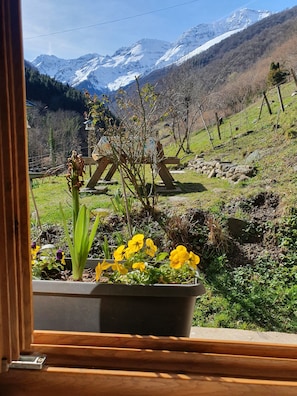 A window view of a mountainous landscape with snow-capped peaks, a garden with yellow flowers, and a wooden fence. - Holiday Home "La Cardabelle" – Nature Retreat in Bonac-Irazein, Private Garden, Mountain Views (Bonac-Irazein)